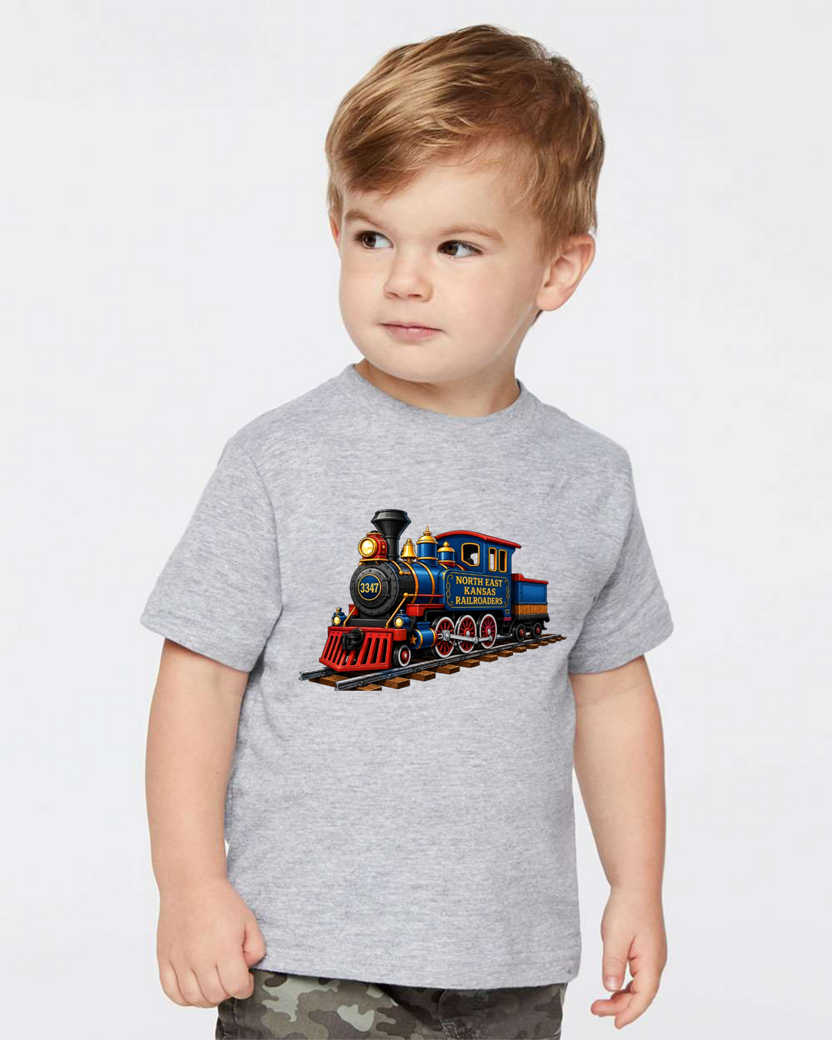 A young child wearing a heather gray short-sleeve t-shirt with a colorful graphic of a vintage steam locomotive train on the front, photographed against a plain light gray studio background.