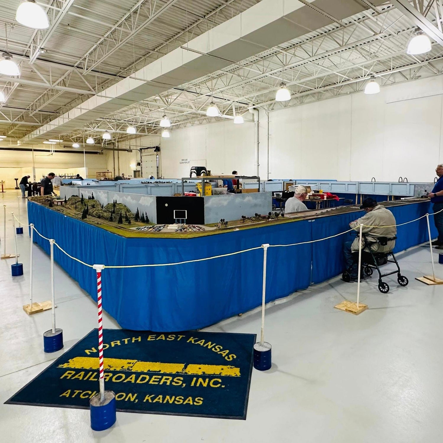 Model train display inside a large indoor facility with 'North East Kansas Railroaders, Inc.' mat.