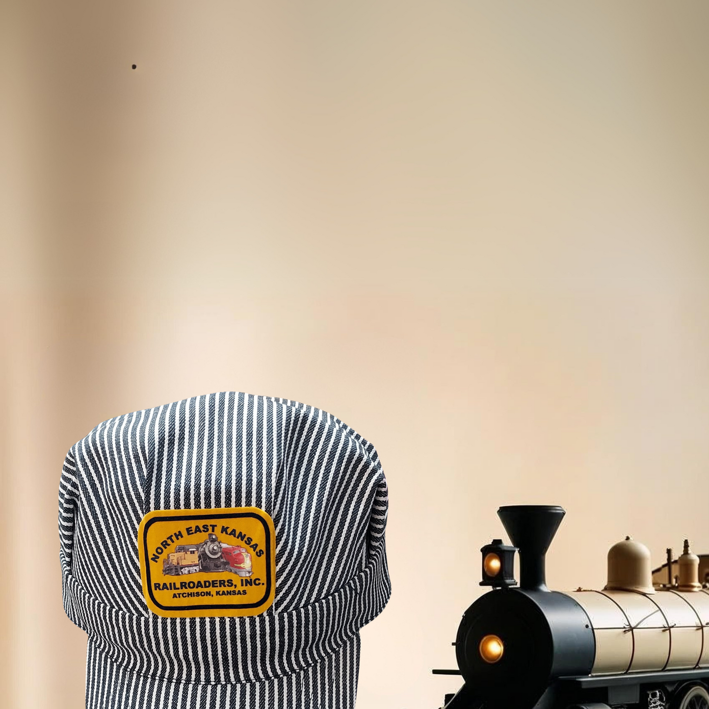 Blue and white striped engineer cap with a logo next to a model train on a wooden surface.