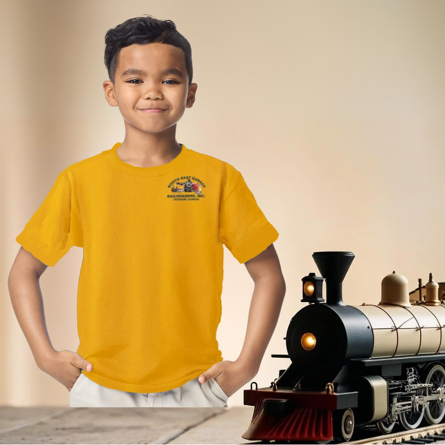 Child wearing a yellow t-shirt with a logo next to a toy train on a beige background