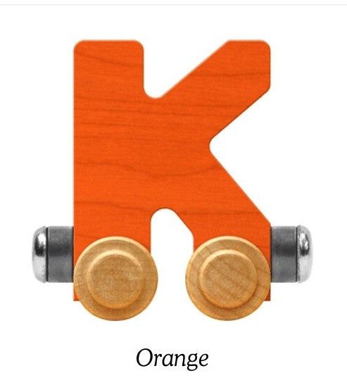 An uppercase letter K wooden toy block in orange wood, featuring two light wood wheels with silver metal axles, shown on a white background with the word 'Orange' printed below.